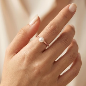 Può includere: Un delicato anello in oro rosa con una singola perla bianca e lucente. La fascia dell'anello è sottile ed elegante, con un design minimalista. La perla è centrata, creando un look classico e raffinato. Un gioiello senza tempo.