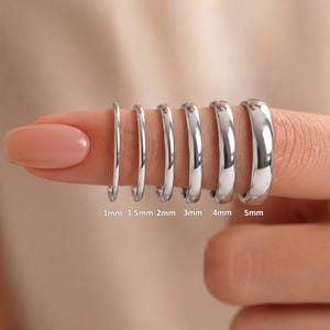 May include: Six polished silver-toned metal rings arranged in a row, ranging in thickness from 1mm to 5mm. The rings are labeled with text indicating their widths: 1mm, 1.5mm, 2mm, 3mm, 4mm, and 5mm, showing a clear progression in size.