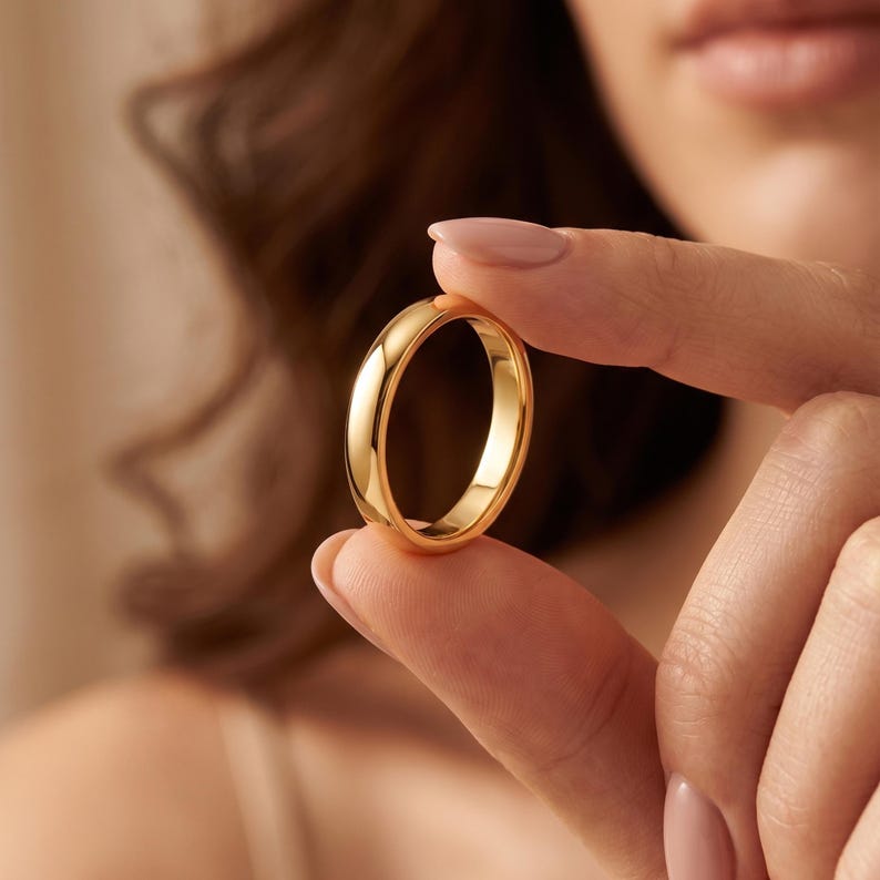 May include: A polished gold band ring with a smooth, rounded surface and a high-shine finish. The ring features a simple, solid construction with a consistent width throughout the entire circular band, reflecting light across its curved exterior.