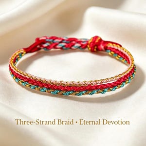 Può includere: Un braccialetto caratterizzato da una treccia a tre fili di colore rosso, verde acqua e oro metallizzato. Il design include una chiusura a nodo e il testo Three-Strand Braid • Eternal Devotion stampato sotto il gioiello sul tessuto.