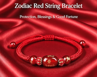 Puede incluir: Una pulsera de hilo rojo con una cuenta central roja con símbolos dorados, flanqueada por dos cuentas rojas más pequeñas con grabados en oro y dos nudos decorativos dorados. El texto dice Zodiac Red String Bracelet Protection, Blessings & Good Fortune.