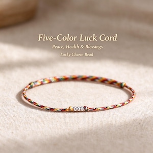 May include: A thin bracelet made of braided cord in five colours, featuring three small silver-toned metallic beads at the centre. The text above reads: Five-Colour Luck Cord, Peace, Health & Blessings, Lucky Charm Bead.