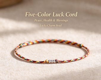 Puede incluir: Una pulsera fina hecha de cordón trenzado en cinco colores, con tres pequeñas cuentas metálicas de tono plateado en el centro. El texto superior dice: Five-Color Luck Cord, Peace, Health & Blessings, Lucky Charm Bead.