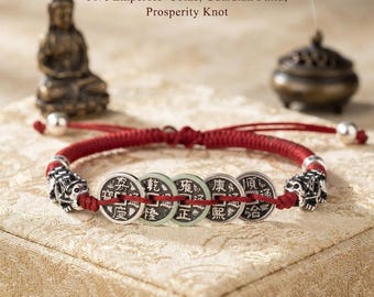 Puede incluir: Una pulsera de cordón rojo con cinco monedas de metal redondas con caracteres chinos, dos dijes Pixiu de tono plateado y cuentas plateadas. El texto Five Emperors' Coins, Guardian Pixiu, Prosperity Knot es visible sobre la pulsera.