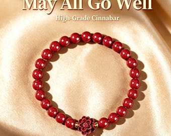 Puede incluir: Una pulsera circular hecha de cuentas de cinabrio rojo intenso con un dije central de flor roja tallada, acentuado por pequeños espaciadores de tono dorado. El texto "May All Go Well" y "High-Grade Cinnabar" aparece sobre la pieza de joyería.