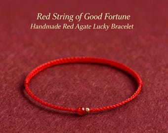 Puede incluir: Una pulsera de cordón rojo fino con una pequeña cuenta de ágata roja y una diminuta cuenta de metal dorado. El texto sobre la pulsera dice: Red String of Good Fortune, Handmade Red Agate Lucky Bracelet. El diseño es sencillo y circular.
