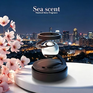 Könnte beinhalten: Ein schwarzer und silberner Lufterfrischer mit einer kugelförmigen Glaskugel, einem Spiraldesign und einem kreisförmigen Sockel. Der Text "Sea scent Nautical Story Fragrance" wird über dem Produkt angezeigt. Rosa Kirschblüten befinden sich im Vordergrund, mit einer Skyline im Hintergrund.