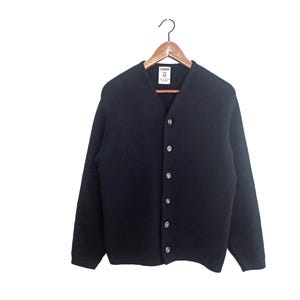 May include: A navy blue cardigan sweater with a V-neck and long sleeves. The sweater has a button-up front with six round, light-colored buttons. It is hanging on a wooden hanger against a white background.