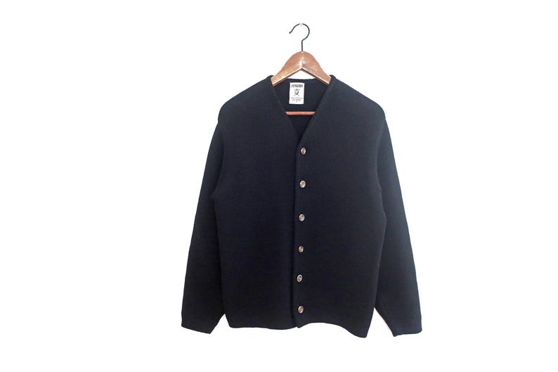 May include: A navy blue cardigan sweater with a V-neck and long sleeves. The sweater has a button-up front with six round, light-colored buttons. It is hanging on a wooden hanger against a white background.