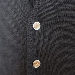 May include: Close-up of a dark gray knitted cardigan with two decorative buttons. The buttons are silver with a gold-colored center. The cardigan has a V-neck and a textured knit pattern.