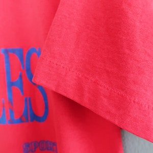 May include: Red t-shirt with a blue and white "Los Angeles" graphic print. The shirt has a ribbed crew neck and short sleeves.