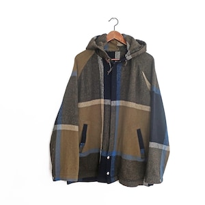 May include: A hooded jacket with a plaid pattern in shades of grey, blue, and tan. The jacket has a front zip closure, two front pockets, and a hood. It is hanging on a wooden hanger against a white background.