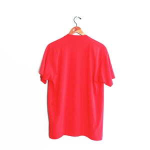 May include: A plain red t-shirt hanging on a wooden hanger against a white background.