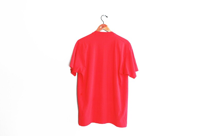 May include: A plain red t-shirt hanging on a wooden hanger against a white background.