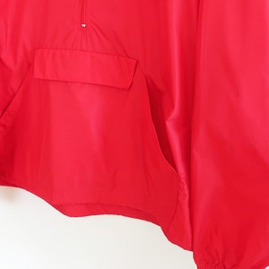 May include: A red windbreaker jacket with a zip closure and a kangaroo pocket. The jacket has long sleeves and a drawstring hood.