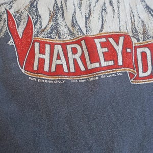 May include: A dark blue t-shirt with a white eagle graphic and a red and white Harley-Davidson logo. The text "FOR BIKERS ONLY P.O. BOX 13888 St. Louis, Mo." is printed below the logo.