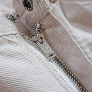 K&ouml;nnte beinhalten: Nahaufnahme eines Rei&szlig;verschlusses an einer beige Cordjacke. Der Rei&szlig;verschluss-Schieber tr&auml;gt den Schriftzug "YKK".