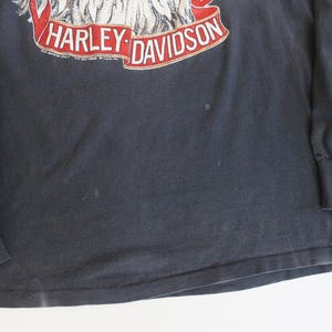 May include: Black long-sleeve t-shirt with a Harley-Davidson eagle graphic and red ribbon accents. The shirt has a distressed look and is made of a soft, comfortable fabric.