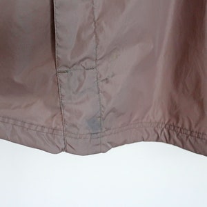Pu&ograve; includere: Una giacca di nylon marrone con chiusura a zip e una piccola tasca sul lato sinistro. La giacca ha un cordoncino in fondo e una cucitura al centro della schiena.