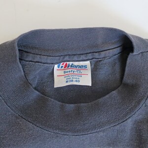 May include: A gray Hanes Beefy-T t-shirt tag with white text that reads "Hanes Beefy-T", "100% Cotton", "Made in U.S.A.", and "M 38-40".