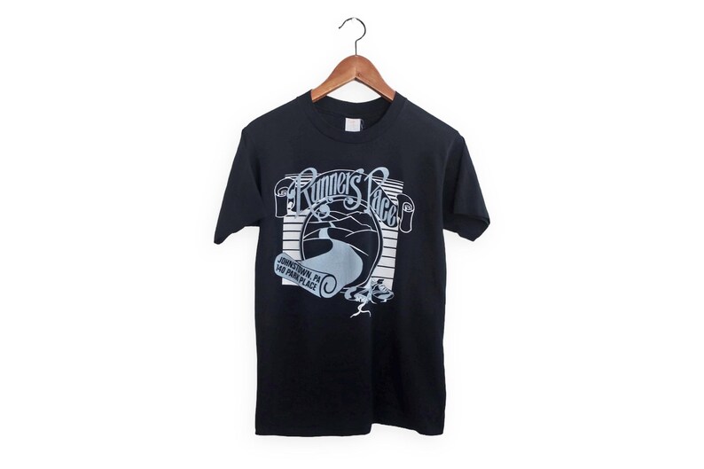 May include: Black t-shirt with a white graphic of "Runner's Place" in a retro style. The graphic includes a winding road and the text "Johnstown, PA 140 Park Place".