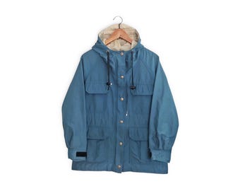 May include: A blue hooded jacket with a zipper closure and multiple pockets. The jacket has a drawstring hood and a brown hanger.