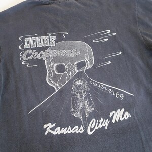 May include: A dark gray long-sleeve t-shirt with a white graphic print of a skull, a motorcycle, and the text "Doug's Choppers", "816 452-8169", and "Kansas City Mo."