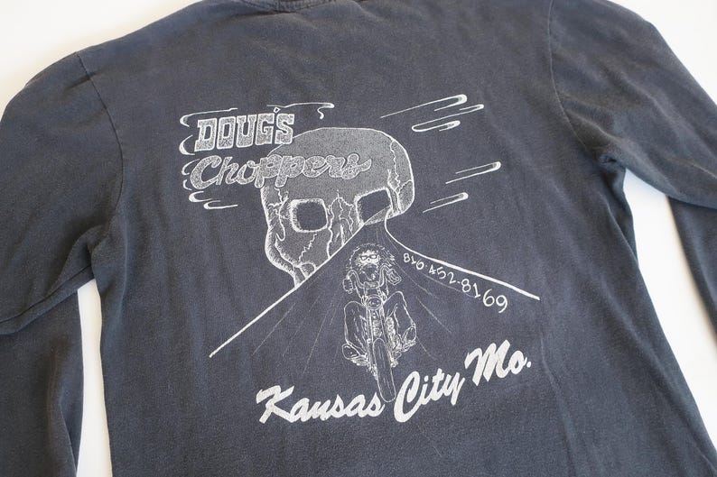 May include: A dark gray long-sleeve t-shirt with a white graphic print of a skull, a motorcycle, and the text "Doug's Choppers", "816 452-8169", and "Kansas City Mo."