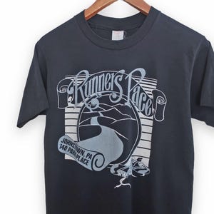 May include: Black t-shirt with a white graphic of a road winding through a landscape with the text "Runner's Pace" and "Johnstown, PA 140 Park Place".