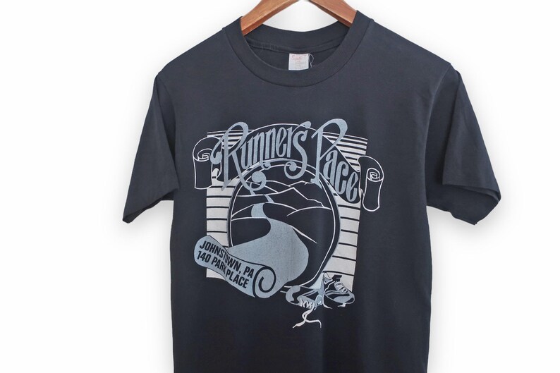 May include: Black t-shirt with a white graphic of a road winding through a landscape with the text "Runner's Pace" and "Johnstown, PA 140 Park Place".
