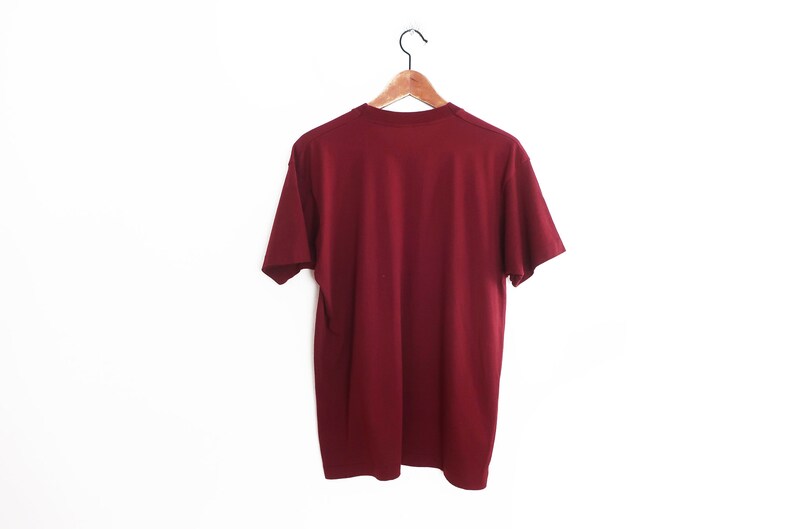 Op de afbeelding: Een effen maron T-shirt hangend aan een houten hanger tegen een witte achtergrond.