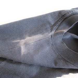 May include: A dark blue t-shirt with a faded white mark on the shoulder.