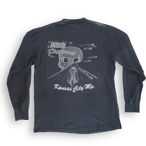 May include: A dark blue long-sleeved t-shirt with a white graphic of a skull riding a motorcycle on a road with the text "DOOGS Choppers" and "Kansas City Mo."