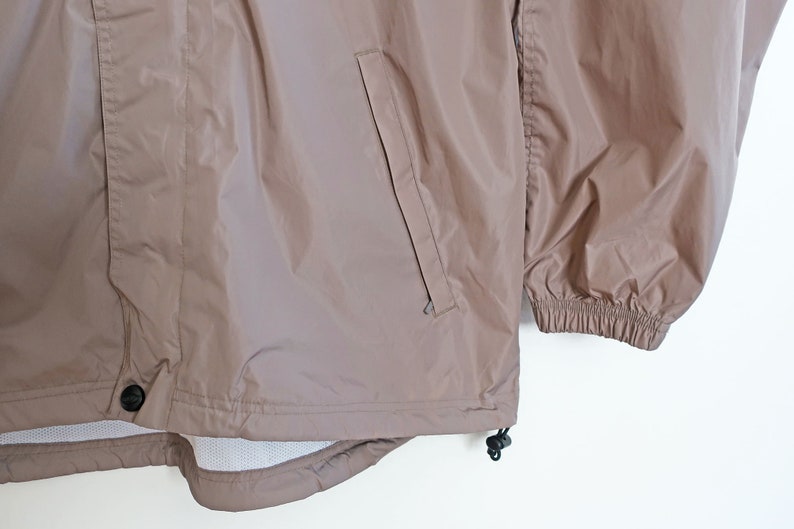 Pu&ograve; includere: Una giacca a vento di colore marrone chiaro con chiusura a zip, una tasca sul lato sinistro e polsini elastici.