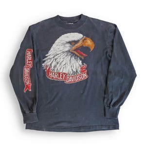 May include: A dark blue long-sleeved t-shirt with a white eagle graphic and the text "Harley Davidson" on the front and sleeve.