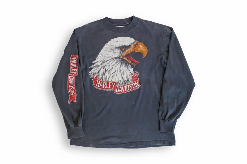 May include: A dark blue long-sleeved t-shirt with a white eagle graphic and the text "Harley Davidson" on the front and sleeve.