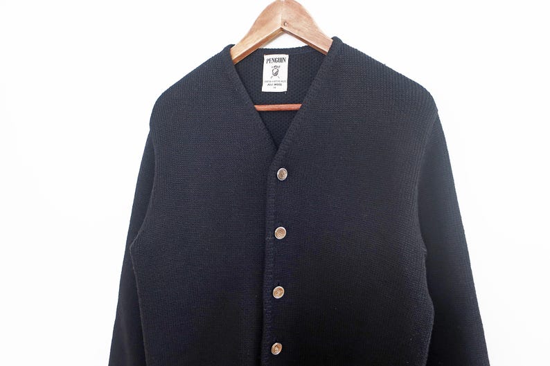 May include: A navy blue cardigan sweater with a V-neck and button closure. The sweater is hanging on a wooden hanger against a white background. The brand label "Penguin" is visible at the neckline.