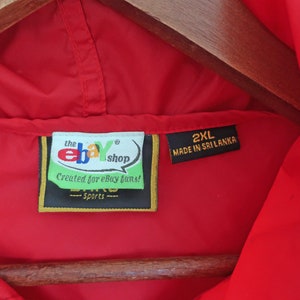 May include: Red hooded jacket with a black label that says "the ebay shop" and "Created for ebay fans!" in white text. The label also has a gold border and the text "Sports" in white text. A second black label says "2XL MADE IN SRI LANKA" in white text.