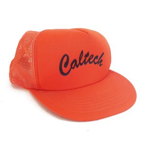 May include: Vibrant orange trucker cap with a curved peak and mesh back. The word "Caltech" is printed in black script. A classic, casual accessory.