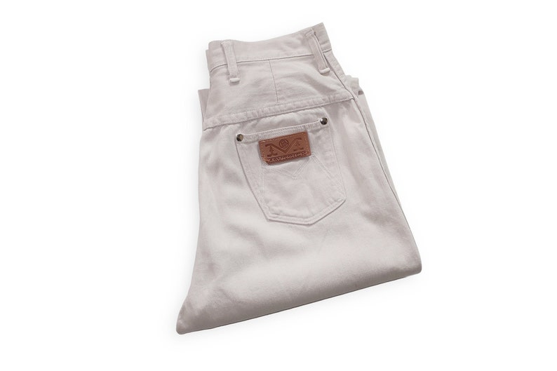 K&ouml;nnte beinhalten: Wei&szlig;e Jeans aus Denim, zusammengefaltet, mit einem braunen Leder-Patch, auf dem "N.O.T.  Rampage" auf der Ges&auml;&szlig;tasche steht.