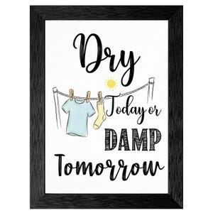 May include: Framed art print with the words "Dry Today or Damp Tomorrow." The image features a clothesline with a light blue t-shirt and a yellow sock hanging from it, with a sun illustration. The frame is black.