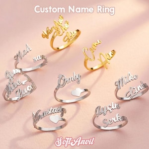 May include: A collection of custom name rings in gold and silver tones. The rings feature various names in a cursive font. Some rings include heart or crown accents. The text "Custom Name Ring" and "Soft Anvil" are also visible.
