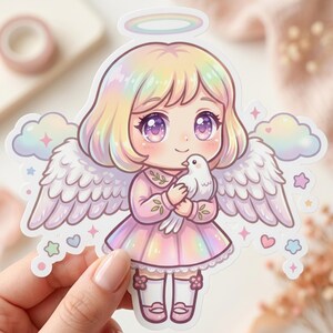 以下が含まれることがあります： 虹色の光輪、翼、ドレスを着た、アニメスタイルの天使のカラフルなステッカー。天使は白い鳩を持っています。パステルカラーと星とハートのアクセントが天使を囲んでいます。