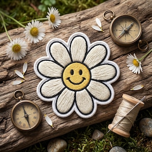 May include: A daisy-shaped embroidered patch with a yellow smiley face center and cream-colored petals. The patch is on a weathered wooden surface, surrounded by daisies, a compass, and a spool of thread, suggesting a craft or nature theme.