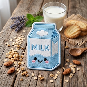 Puede incluir: Un parche bordado rectangular con forma de cartón de leche en tonos azul claro y blanco. El parche presenta la palabra MILK en letras azules, un icono de nube blanca y una cara sonriente con mejillas rosadas en la parte inferior.