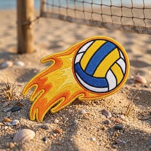 May include: An embroidered patch featuring a volleyball with blue, yellow, and white panels. The ball is depicted with a trail of stylised orange and yellow flames extending behind it, creating a sense of motion. The design has a thick yellow border.