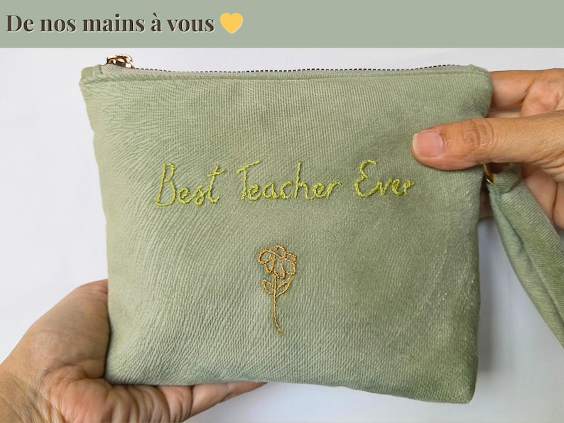 Op de afbeelding: Saliegroene etui met gouden rits en polsbandje, geborduurd met "Best Teacher Ever" in geelgroen schrift en een gouden bloem. De tekst "De nos mains &agrave; vous" staat bovenaan.