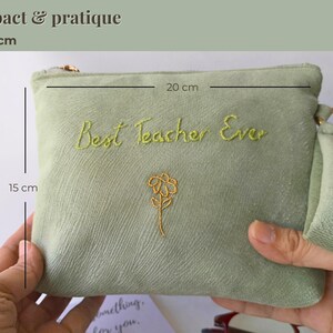 Op de afbeelding: Een saliegroene etui met de geborduurde tekst "Best Teacher Ever" en een gouden bloemdesign. De etui meet 20 cm x 15 cm en heeft een gouden rits en een klein handvat.