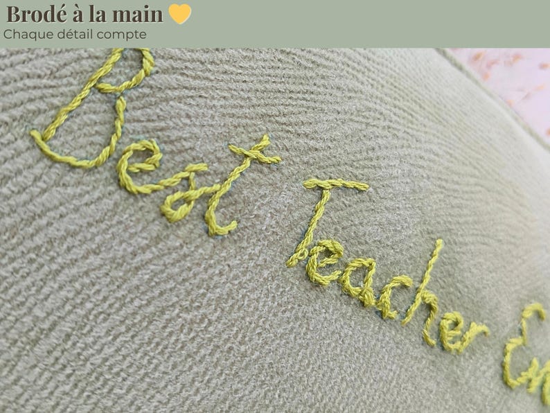 Op de afbeelding: Close-up van een lichtgroene stof met gele geborduurde tekst die luidt "Best Teacher Ever". De woorden "Brode a la main" en "Chaque detail compte" staan boven de tekst.