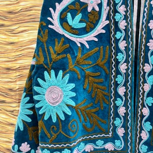 K&ouml;nnte beinhalten: T&uuml;rkisblaue Samtjacke mit aufwendiger Blumenstickerei in Hellblau, Braun und Rosa. Die Jacke zeigt ein detailliertes Muster aus Blumen und Bl&auml;ttern, mit einem kontrastierenden schwarzen Futter an den R&auml;ndern.